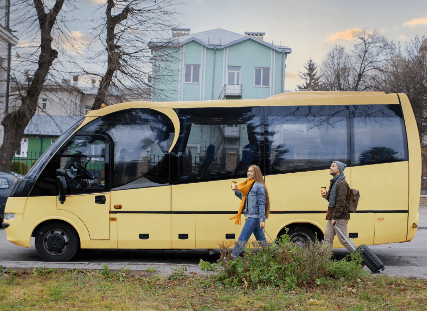 Sarı renkli minibüs ve yanında valizli iki yolcu